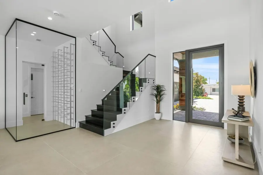 A bright foyer with a glass wine room, a glass stair rail and a glass entry door